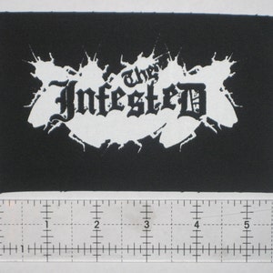 May include: Black and white embroidered patch with the text "The Infested" in a gothic font.