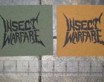 May include: Two black and white embroidered patches with the text "Insect Warfare" on a green and brown fabric background.