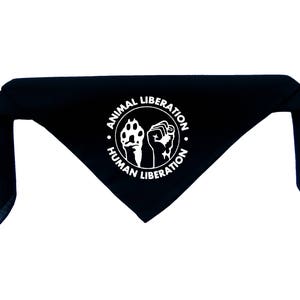 Puede incluir: Bandana negra con un diseño circular blanco que presenta una huella de pata y un puño con el texto "Liberación animal Liberación humana".