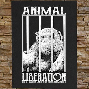 以下が含まれることがあります： 檻の中にいる猿の白黒のイラストで、"ANIMAL LIBERATION ZOO CAGES ARE NOT CONSERVATION"というテキストが書かれています。