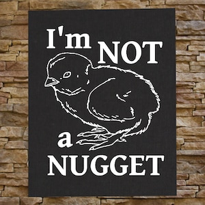 以下が含まれることがあります： 「I'm NOT a NUGGET」というテキストと、ヒヨコの漫画の画像が描かれた白黒の看板。
