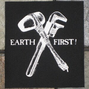 May include: Black and white patch with a crossed hammer and wrench. The text "EARTH FIRST!" is printed below the tools.