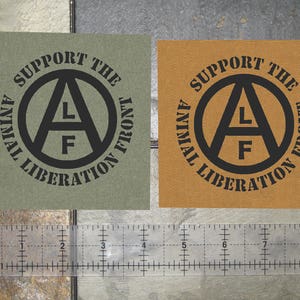 May include: Two fabric patches with the text "Support the Animal Liberation Front" and a black anarchy symbol with the letters "ALF" inside. The patches are on a brown and gray background.