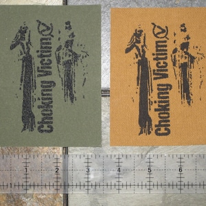 May include: Two fabric patches with black ink depicting two figures and the text "Choking Victim". The patches are on a green and a brown background.
