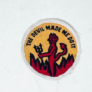 May include: Round patch with a yellow center and white border. The patch features a red devil holding a trident, standing above red flames. The text "THE DEVIL MADE ME DO IT" is in black around the edge.
