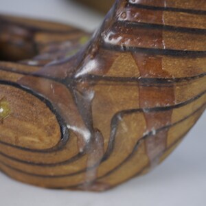 May include: Close-up of a wooden sculpture with a brown and black striped pattern. The sculpture is covered in a clear, viscous substance that is dripping down the sides.
