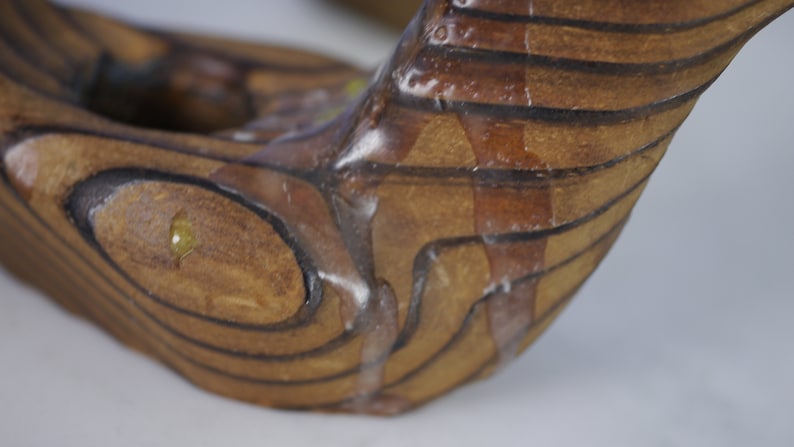 May include: Close-up of a wooden sculpture with a brown and black striped pattern. The sculpture is covered in a clear, viscous substance that is dripping down the sides.