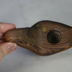 May include: A wooden fish-shaped object with a hole in the center. The wood is dark brown and has a grain pattern. The object is carved in a stylized shape.