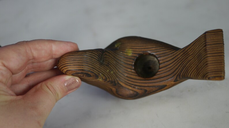 May include: A wooden fish-shaped object with a hole in the center. The wood is dark brown and has a grain pattern. The object is carved in a stylized shape.