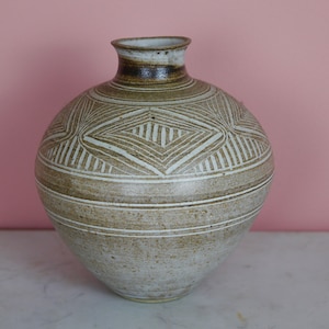 May include: A white ceramic vase with a brown glaze and a geometric pattern. The vase has a round body and a narrow neck.