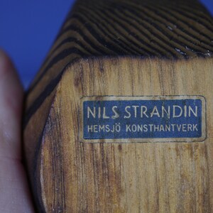 May include: A wooden sculpture with a blue label that reads "NILS STRANDIN HEMSJ&Ouml; KONSTHANTVERK".