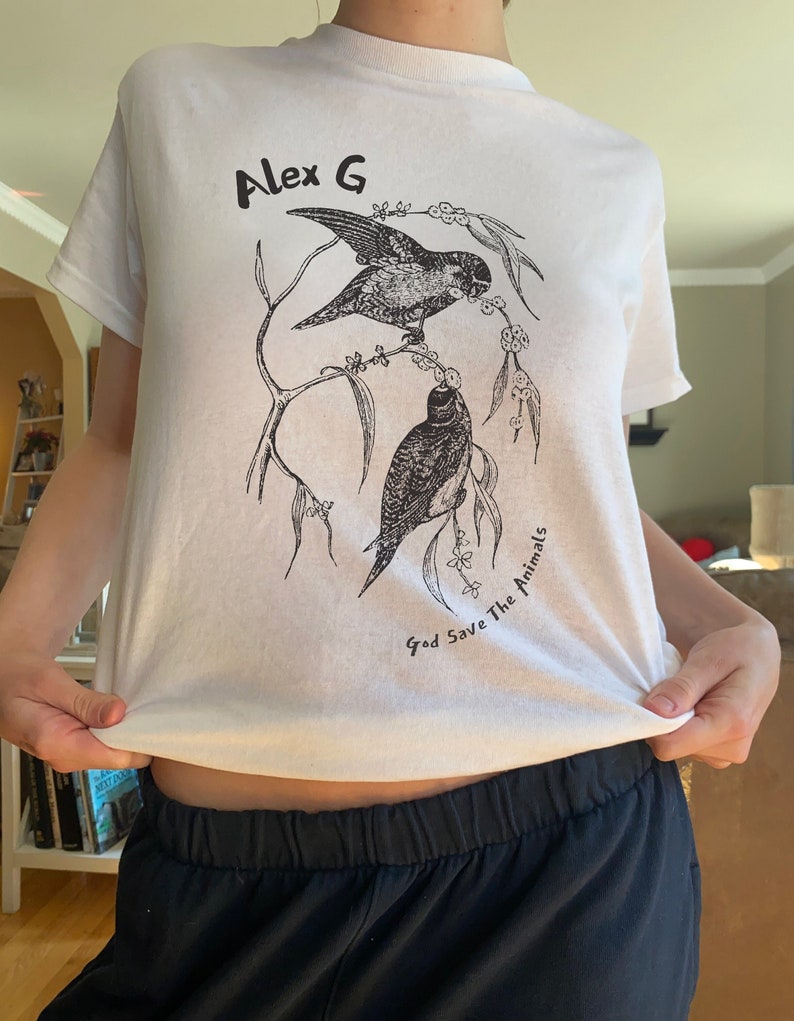 Alex G Merch Shirt featuring two birds on a branch together and the text "Alex G, God Save The Animals" for his latest album.