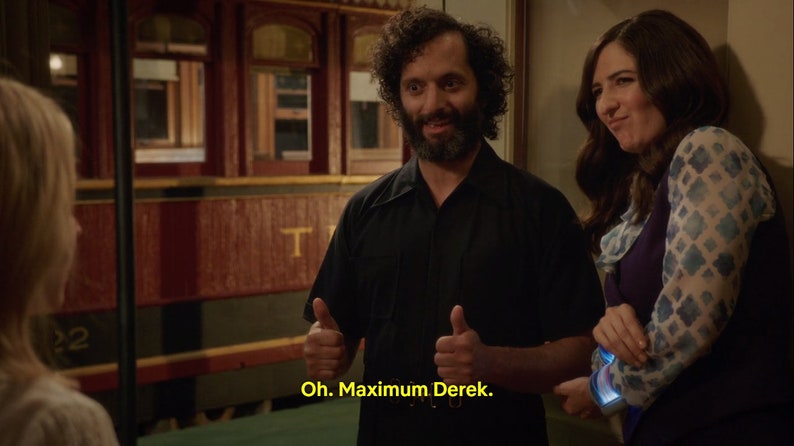 May include: A man with a beard and a black shirt gives a thumbs up to a woman with long brown hair wearing a purple top and a blue and white patterned shirt. The woman is smiling and looking at the man. The man is saying "Oh. Maximum Derek."