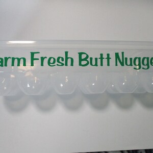 May include: A clear plastic egg carton with the text "Farm Fresh Butt Nuggets" printed in green letters.