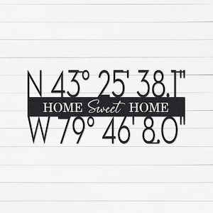Peut inclure: Décoration murale en métal noir avec l'inscription "HOME Sweet HOME" et les coordonnées : N 43° 25' 38.1" et W 79° 46' 8.0". Le signe est placé sur un fond de planches de bois blanches. Un élément décoratif pour la maison.