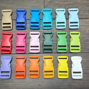 Könnte beinhalten: Eine Sammlung farbenfroher Kunststoffschnallen in verschiedenen Farbtönen, darunter Beige, Blau, Rot, Rosa, Lila, Orange, Gelb, Grün und Weiß. Die Schnallen sind auf einer Holzoberfläche angeordnet.