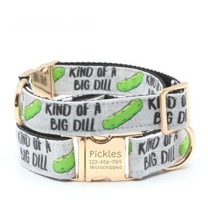 Könnte beinhalten: Ein hellgraues Haustierhalsband mit einem sich wiederholenden Muster aus grünen Gewürzgurken und dem schwarzen Text "KIND OF A BIG DILL". Das Halsband hat eine goldfarbene Metallschnalle mit der Gravur "Pickles", einer Telefonnummer und "Microchipped".