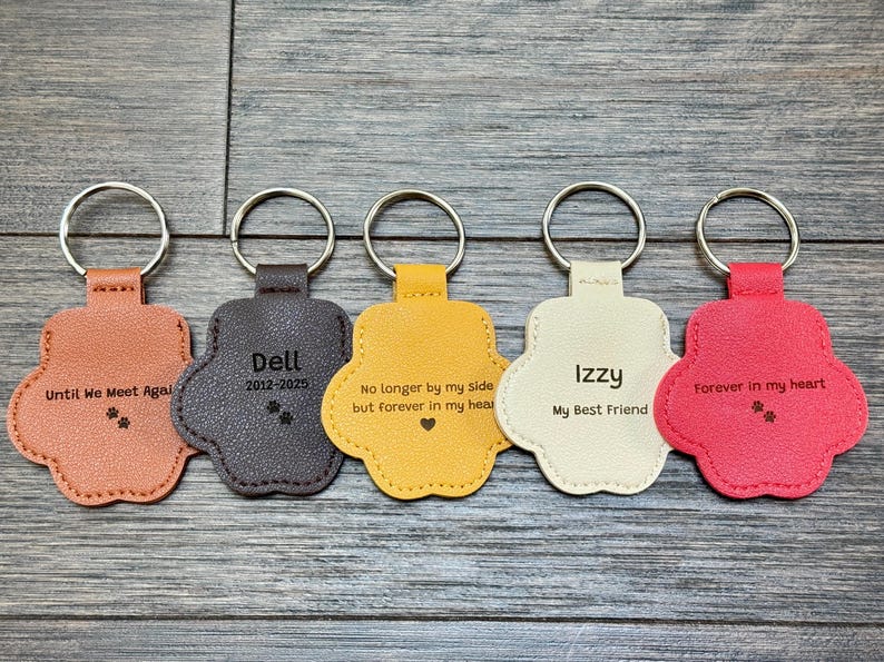 May include: Five paw-shaped keychains in shades of orange, gray, yellow, cream, and red. Each keychain has a silver ring and features engraved text, including names and phrases like "Until We Meet Agal" and "Forever in my heart."