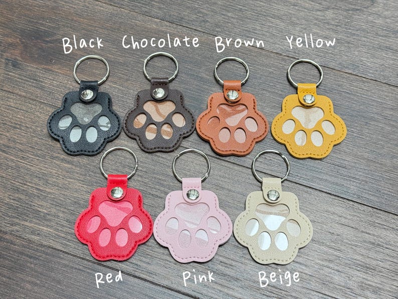 May include: A collection of paw-shaped keychains in various colors: black, chocolate, brown, yellow, red, pink, and beige. Each keychain has a clear window and a metal keyring. The text "Black Chocolate Brown Yellow Red Pink Beige" is written above and below the keychains.