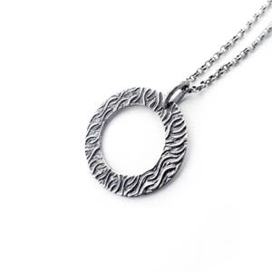 May include: A silver necklace with a textured circular pendant. The pendant has a wavy pattern.