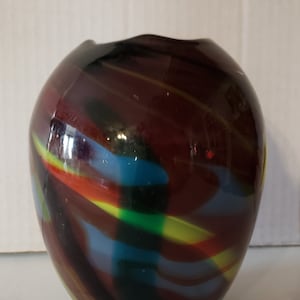 Puede incluir: Un jarrón de vidrio redondo con un patrón de espiral en tonos de rojo, amarillo, azul, verde y negro.
