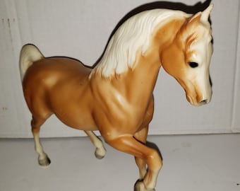 May include: A brown plastic toy horse with a white mane and tail. The horse is standing on all four legs and has its head turned to the side.