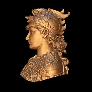 May include: A gold-colored bust sculpture of a person wearing a helmet with intricate details. The sculpture is in profile view and the person's face is visible.