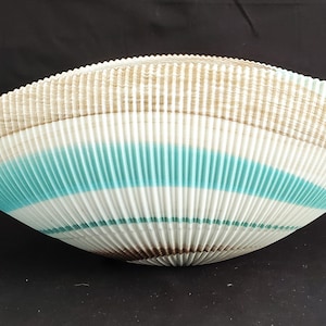 May include: A decorative bowl with a unique, ridged design. The bowl features alternating bands of white, light blue, and tan colors. The bowl's shape is oval, with a wide opening and a shallow depth. The bowl is likely made of ceramic or a similar material.