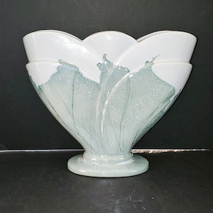 Könnte beinhalten: Eine weiße Keramikvase mit einem abstrakten Design in Grün und Weiß. Die Vase hat eine breite, gewellte Öffnung und einen runden Boden.