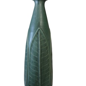 May include: A tall, teal-colored ceramic vase with a leaf design. The vase has a narrow neck and a wide base, with a textured surface. The leaf pattern is carved into the surface of the vase, adding visual interest.