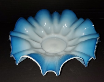 Puede incluir: Un tazón de vidrio blanco y azul con un borde festoneado. El tazón está hecho de vidrio iridiscente y tiene un degradado de color de blanco a azul.