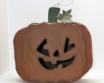 Könnte beinhalten: Ein hölzerner Kürbis mit einem geschnitzten Jack-o'-Lantern-Gesicht. Der Kürbis ist braun bemalt und hat einen grünen Stiel und ein Blatt.