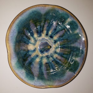 May include: A teal and white ceramic bowl with a raised center and a glazed finish. The bowl has a unique, swirling pattern.