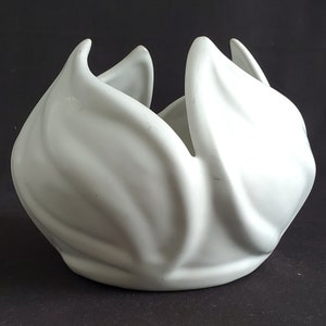 Op de afbeelding: Witte keramische bloempot in de vorm van een gestileerde bloem met vijf bloemblaadjes.