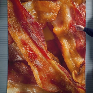May include: Close-up of crispy, cooked bacon strips. The bacon is arranged in a random pattern, with some strips overlapping others. The bacon is a deep golden brown color and has a glossy sheen.