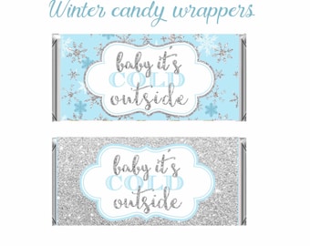 May include: Two candy bar wrappers with a winter theme. One wrapper has a light blue background with snowflakes and the text "baby it's cold outside". The other wrapper has a silver glitter background with the same text.