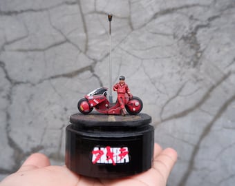 May include: A red and black motorcycle figurine with a rider in a red jumpsuit. The figurine is on a black base with the word "AKIRA" printed on it.