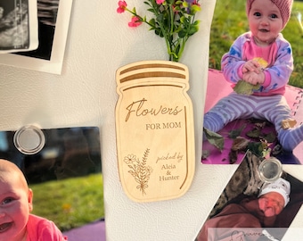 May include: Wooden cutout of a mason jar with the text "Flowers for Mom" and "picked by Aleia & Hunter". The jar is decorated with a floral design and is surrounded by a bouquet of pink and purple flowers.