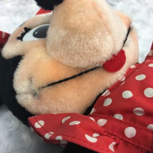 May include: Close-up of a red and white polka dot dress on a plush toy with black ears and a red nose. The toy has large black eyes and a black mouth.