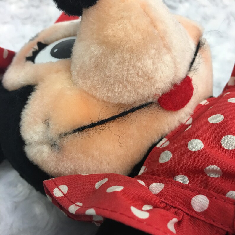 May include: Close-up of a red and white polka dot dress on a plush toy with black ears and a red nose. The toy has large black eyes and a black mouth.