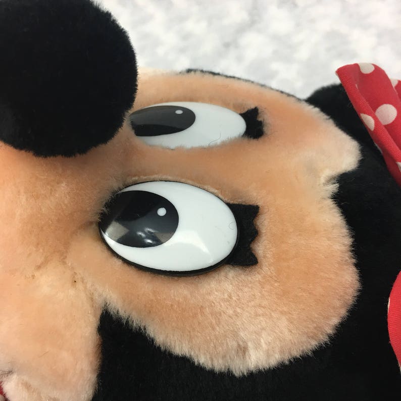 May include: Close-up of a plush Mickey Mouse toy with large, black eyes and a red bow with white polka dots.