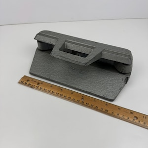 Op de afbeelding: Een grijze metalen papierpons met een handvat en drie gaten. De pons is aan de voorkant gemarkeerd met "Rexel".