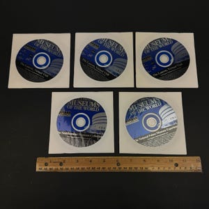 Puede incluir: Cinco CD en fundas de papel blanco, cada uno con un diseño azul y blanco con el texto "Museos del Mundo". Los CD están etiquetados con diferentes colecciones de museos, incluyendo "El Louvre, visita virtual", "The Smithsonian Museum Collection" y "The National Palace Museum Experience".