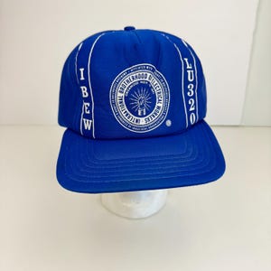 Könnte beinhalten: Eine blaue und weiße Baseballkappe mit dem Text "IBEW" und "LU320" an den Seiten und einem weißen Kreis mit dem Text "International Brotherhood of Electrical Workers" und "Organized Nov. 1891" in der Mitte.