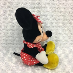 May include: A plush Minnie Mouse toy wearing a red and white polka dot dress with a red bow. She has black ears and a black nose. Her feet are yellow.
