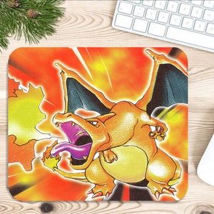 May include: A rectangular mousepad featuring a vibrant illustration of Charizard, a popular fire and flying-type Pokémon. The design showcases Charizard breathing fire against a fiery orange and yellow background. A white mouse and keyboard are visible.