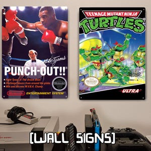 May include: Two rectangular metal wall signs featuring vintage video game box art. The left sign displays Mike Tyson's Punch-Out!! with a boxer and referee. The right sign shows Teenage Mutant Ninja Turtles with four green turtles in action.