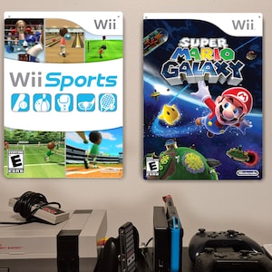 May include: Two framed Wii game posters: "Wii Sports" and "Super Mario Galaxy." The "Wii Sports" poster features game screenshots and the game's logo. The "Super Mario Galaxy" poster shows Mario in space. A console and controllers are visible below.