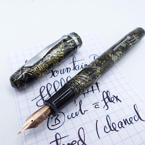 Op de afbeelding: Een zwarte en gouden vulpen met een flexibele punt. De pen heeft een zwart en gouden marmerpatroon en een zilveren dop. De pen ligt op een vel grafiekpapier met de woorden "vulpen" en "flex" erop geschreven.