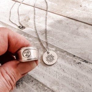 May include: A silver ring with a moon face design and a silver necklace with a sun face pendant. Both pieces of jewelry have a vintage aesthetic.